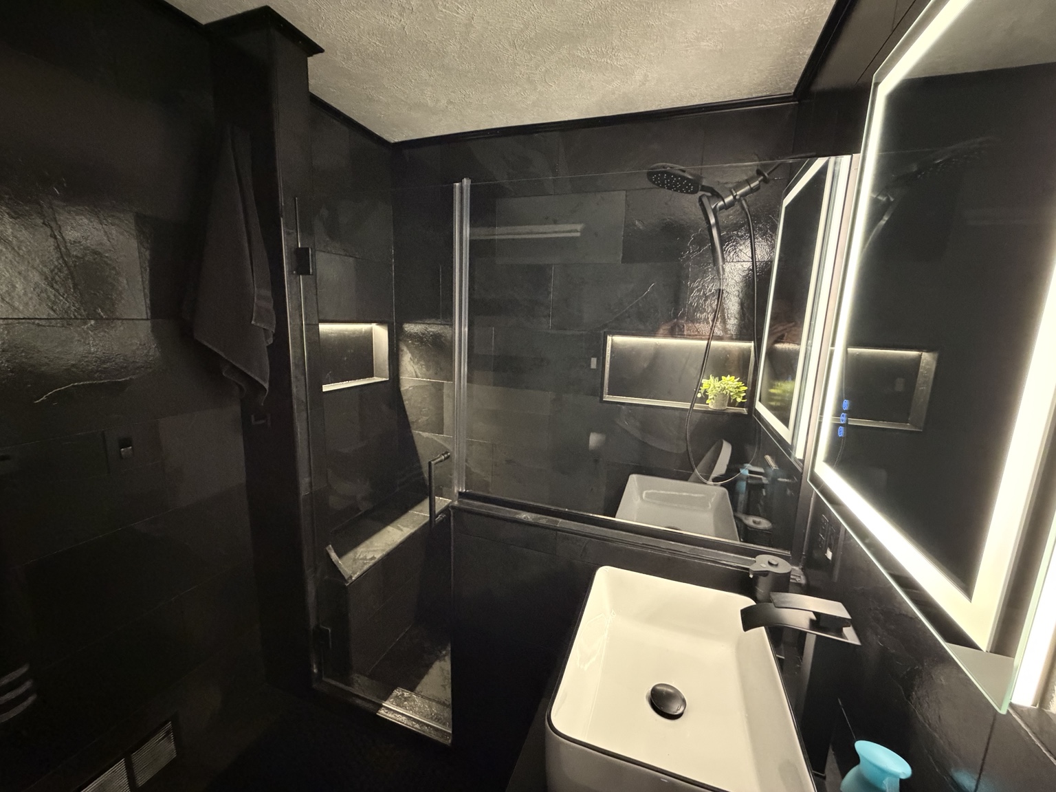 Wide view of the completed black tile bathroom and glass shower