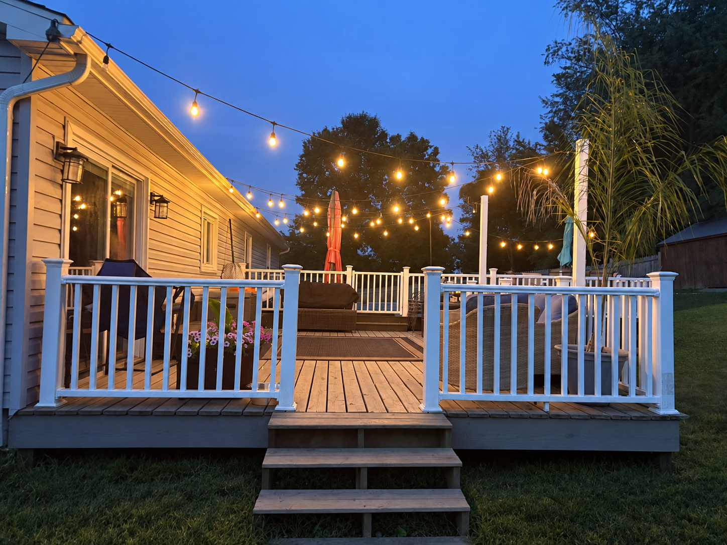 Completed outdoor deck with new white railings and wood steps under warm string lights