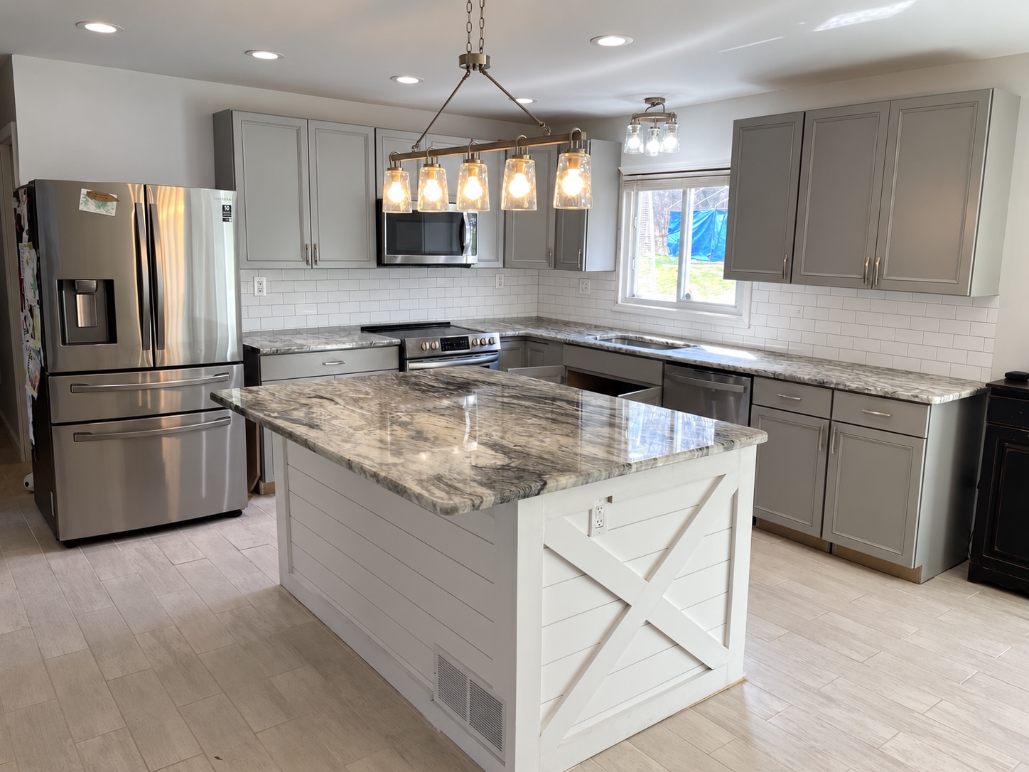 Finished kitchen with gray cabinetry, a large stone island, white tile backsplash, and modern lighting