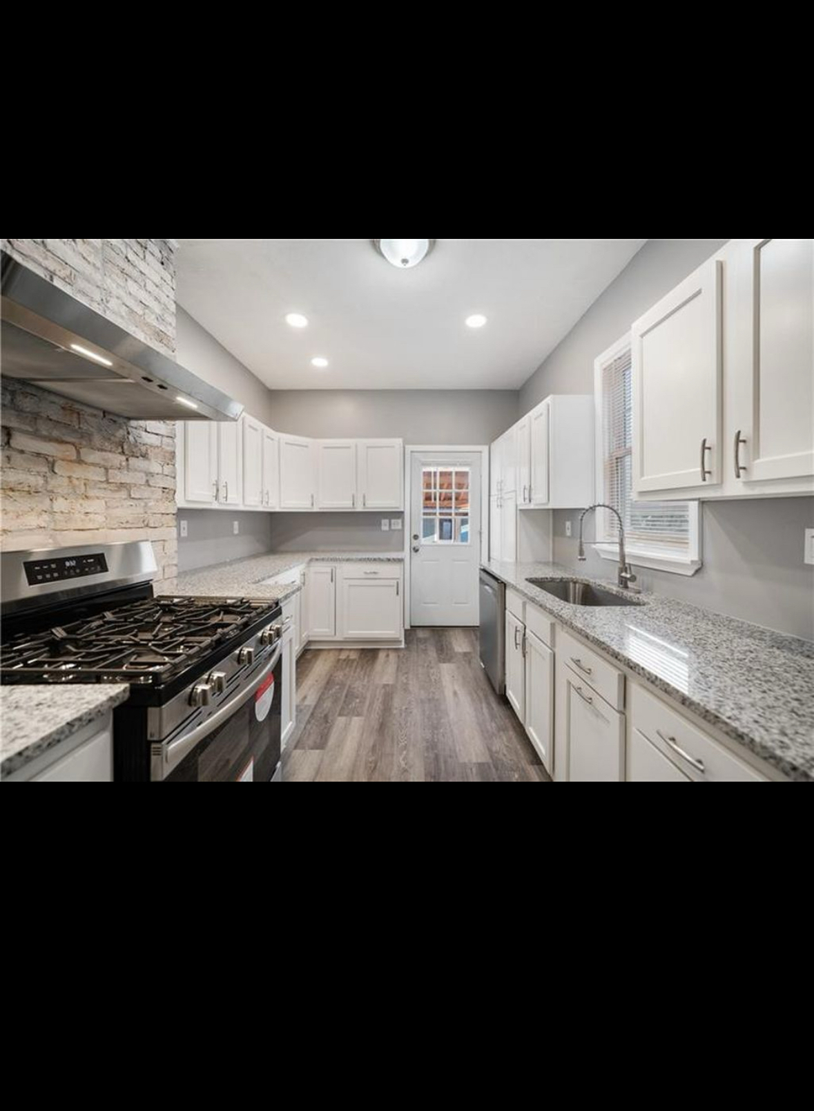 Kitchen after renovation with white cabinets, stone countertops, new flooring, and updated lighting