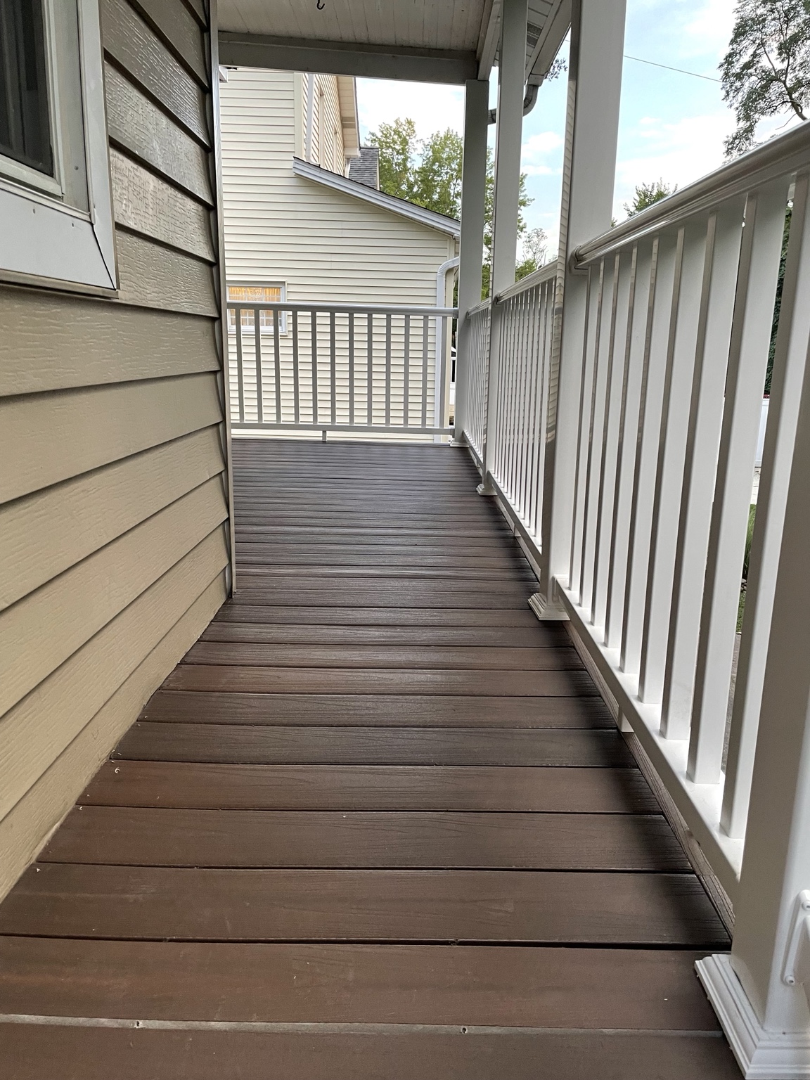 New deck surface and white railing along the side of a home